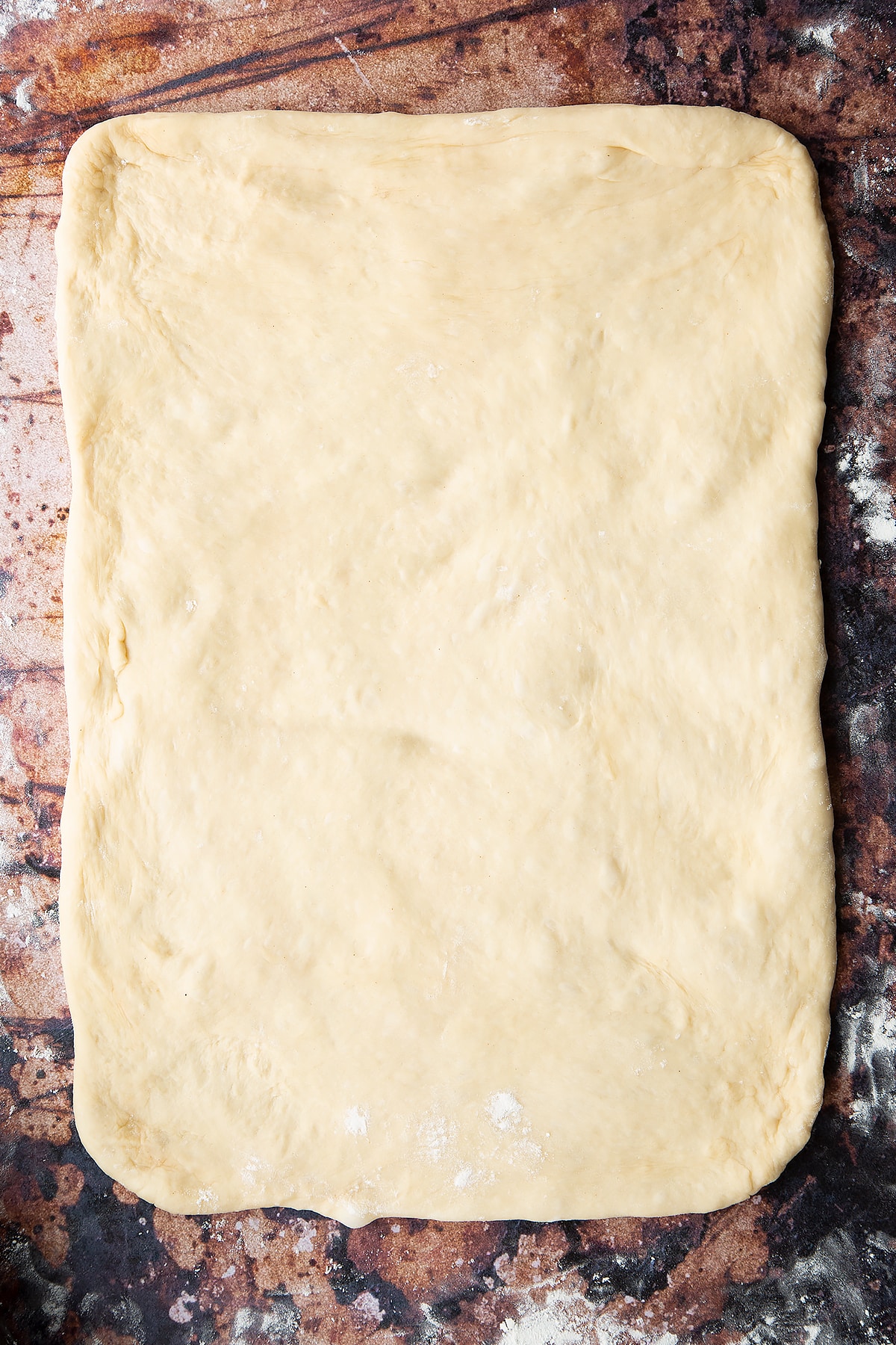 Overhead shot of dough rolled out to create a large rectangle on a floured surface