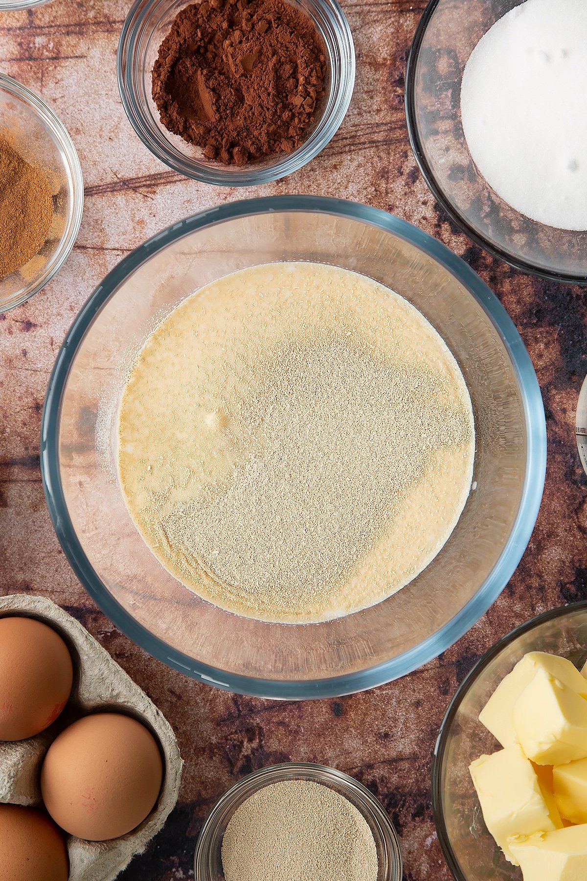 Overhead shot of milk with sugar and yeast in a large clear bowl