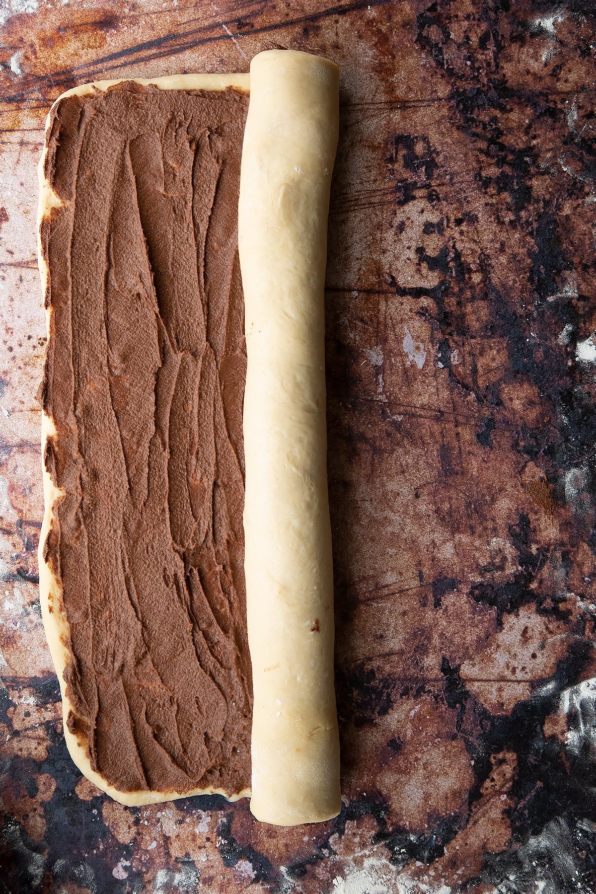 Overhead shot of dough layered with chocolate spread and rolled on one side.