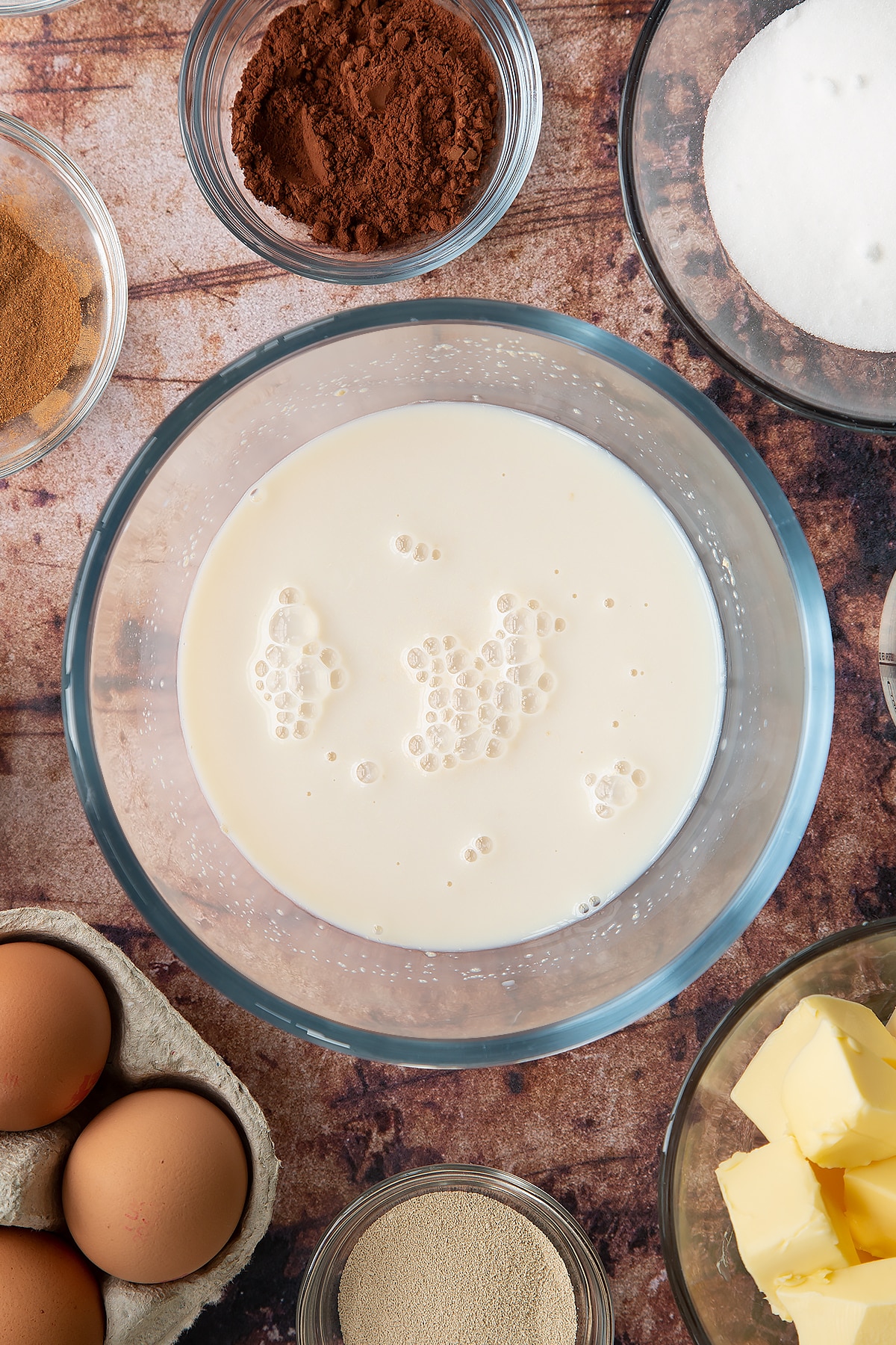 Overhead shot of milk, yeast and sugar mixed together in a large clear bowl.