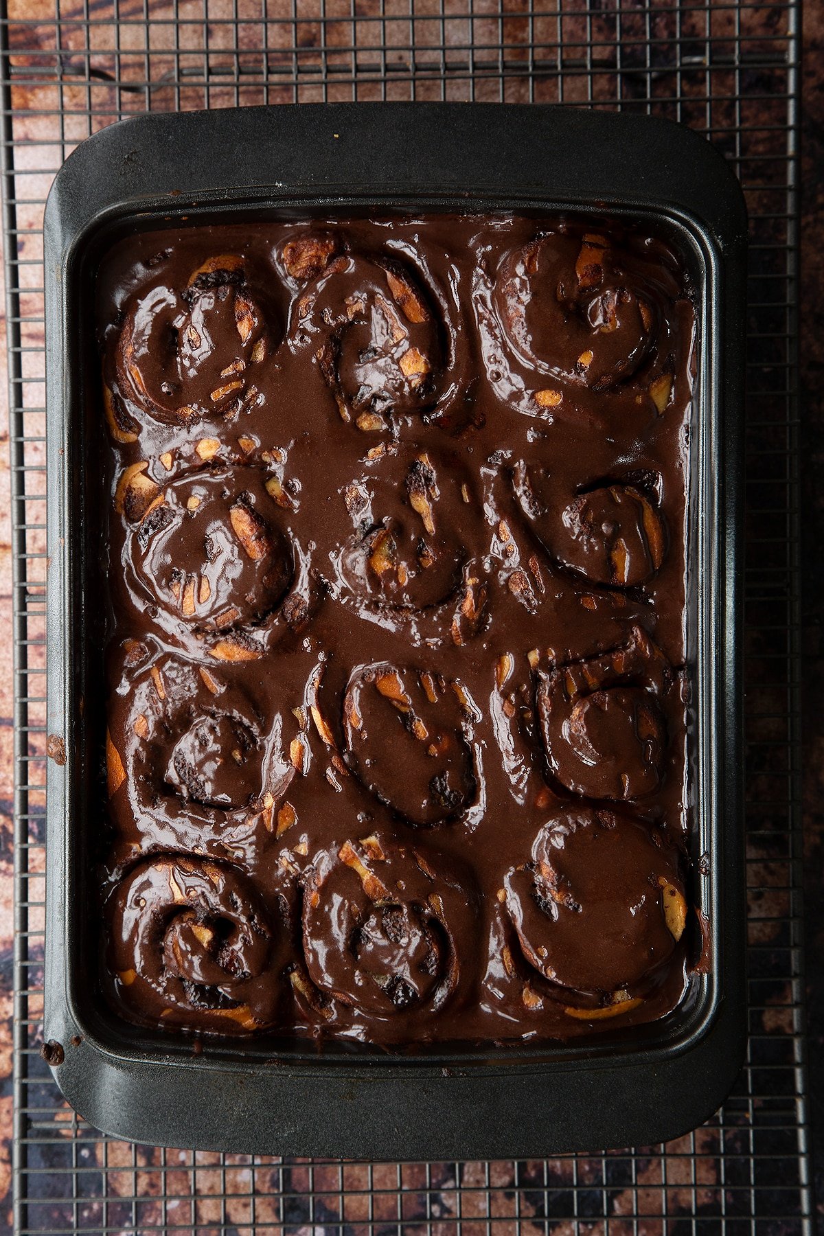 Overhead shot of chocolate cinnamon buns baked in a baking tray covered in chocolate sauce