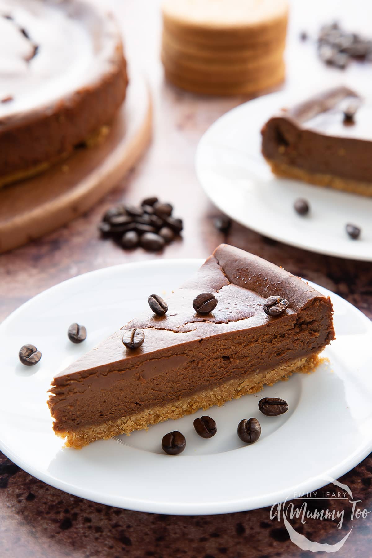 Front view shot of a piece of coffee cheesecake topped with coffee beans on a white plate with the A Mummy Too logo in the corner