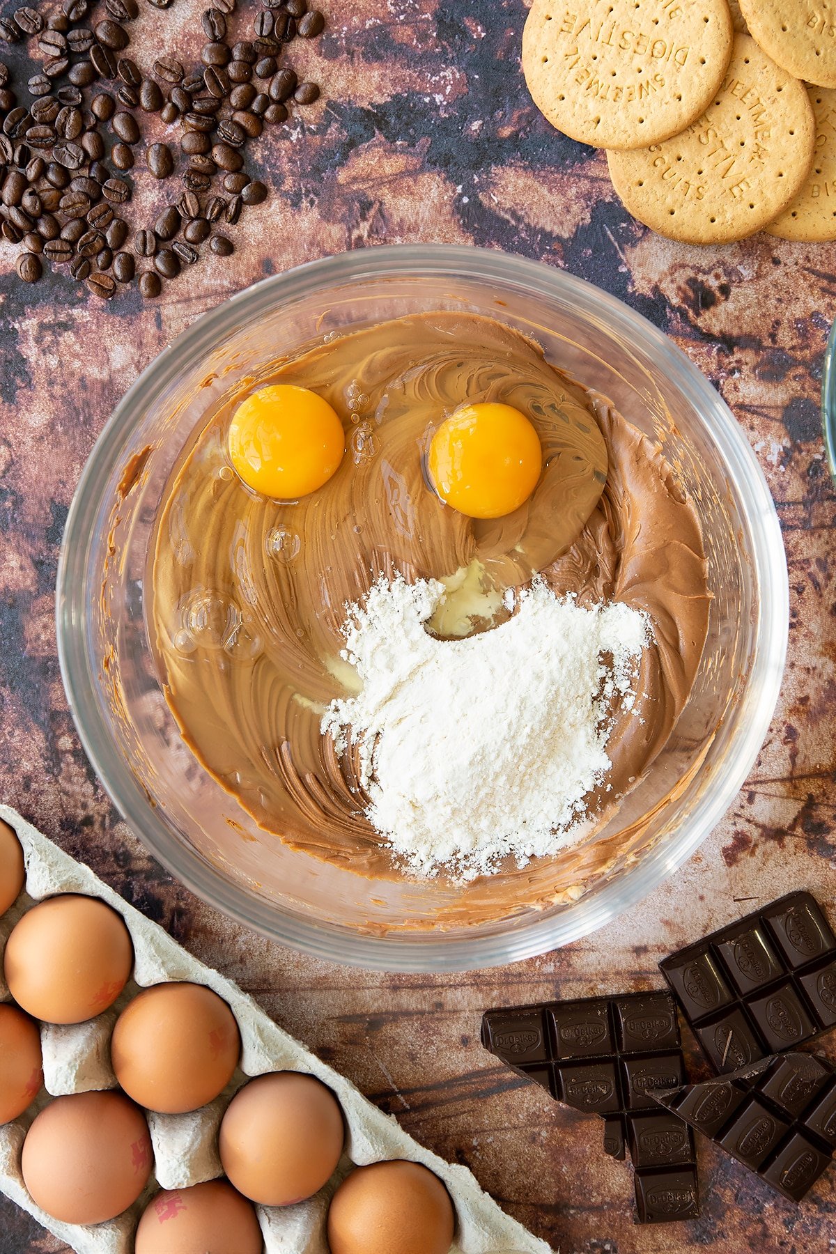 Overhead shot of coffee cheesecake mix with flour and two eggs in a large clear bowl