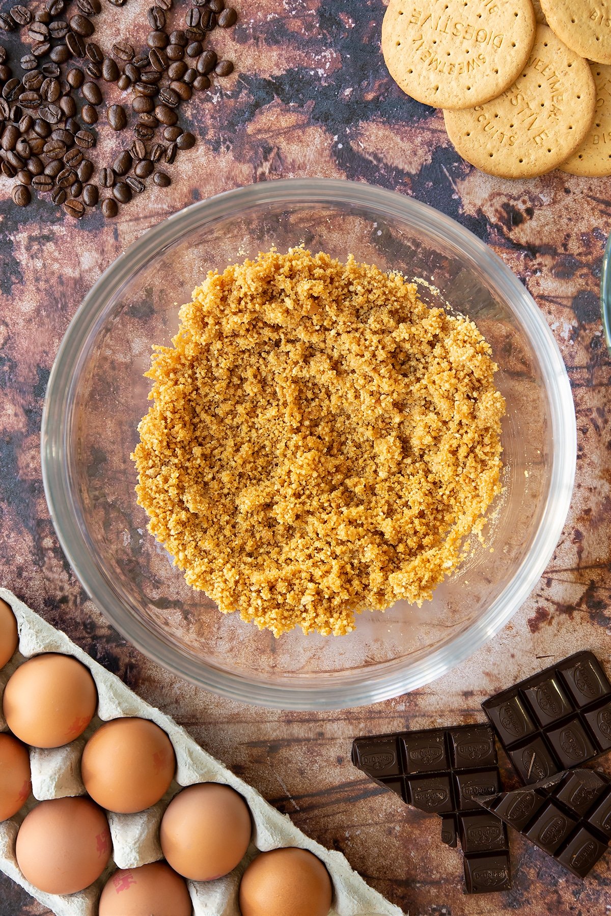 Overhead shot of digestive biiscuit crumb and butter mixed together in a large clear bowl