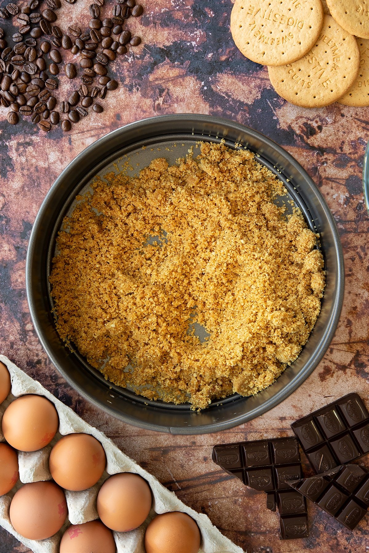 Overhead shot of butter and biscuit crumb mix in a large metal cake tin