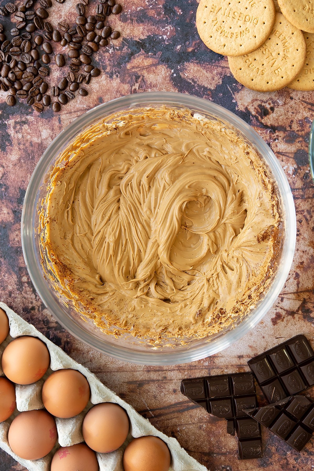Overhead shot of cream cheese, cream, instant coffee and sugar mixed together in a large clear bowl