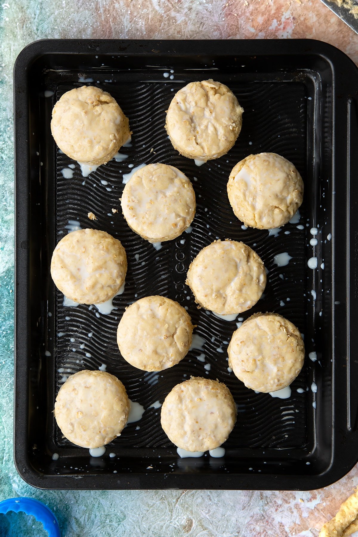 Oatmeal scone rounds of dough brushed with milk on a baking tray. 