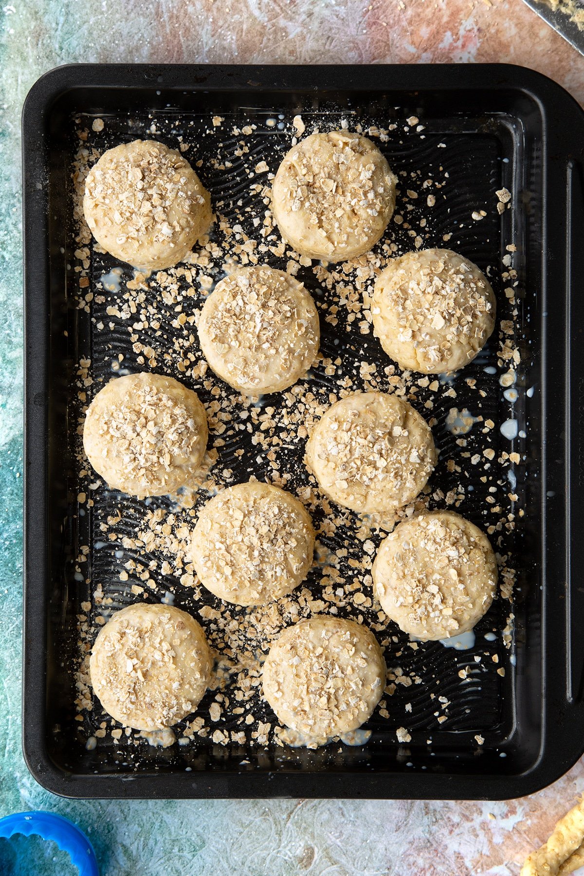 Oatmeal scone rounds of dough, brushed with milk and scattered with oats on a baking tray. 