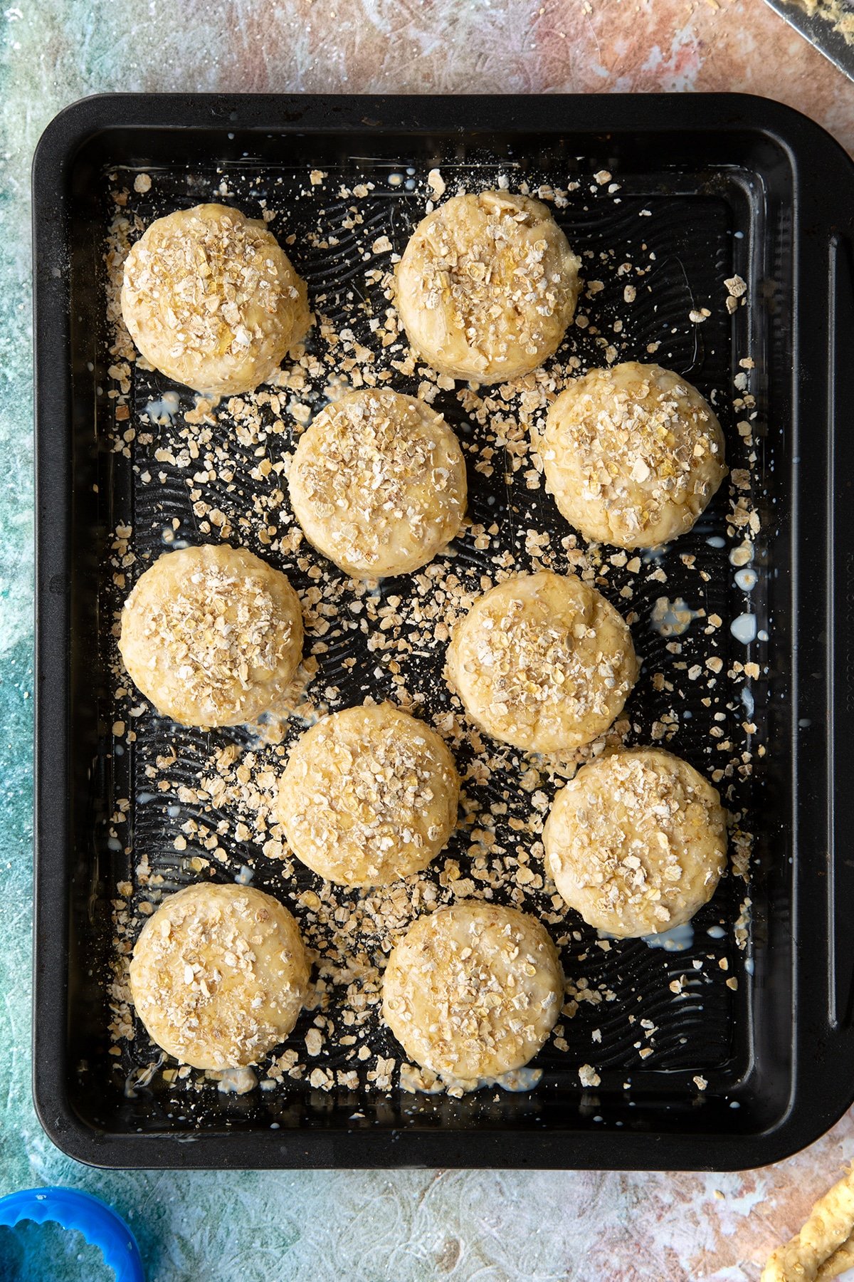 Oatmeal scone rounds of dough, brushed with milk, scattered with oats and drizzled with honey on a baking tray. 