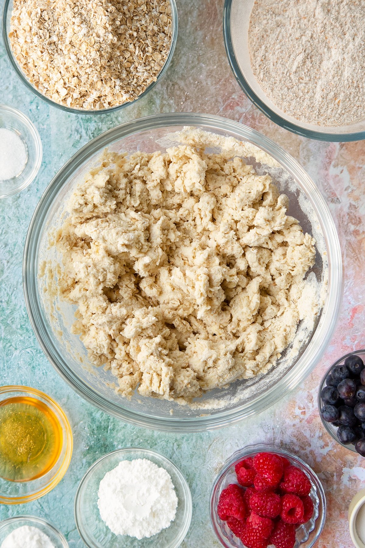 Oatmeal scone dough in a glass mixing bowl. Ingredients to make oatmeal scones surround the bowl.