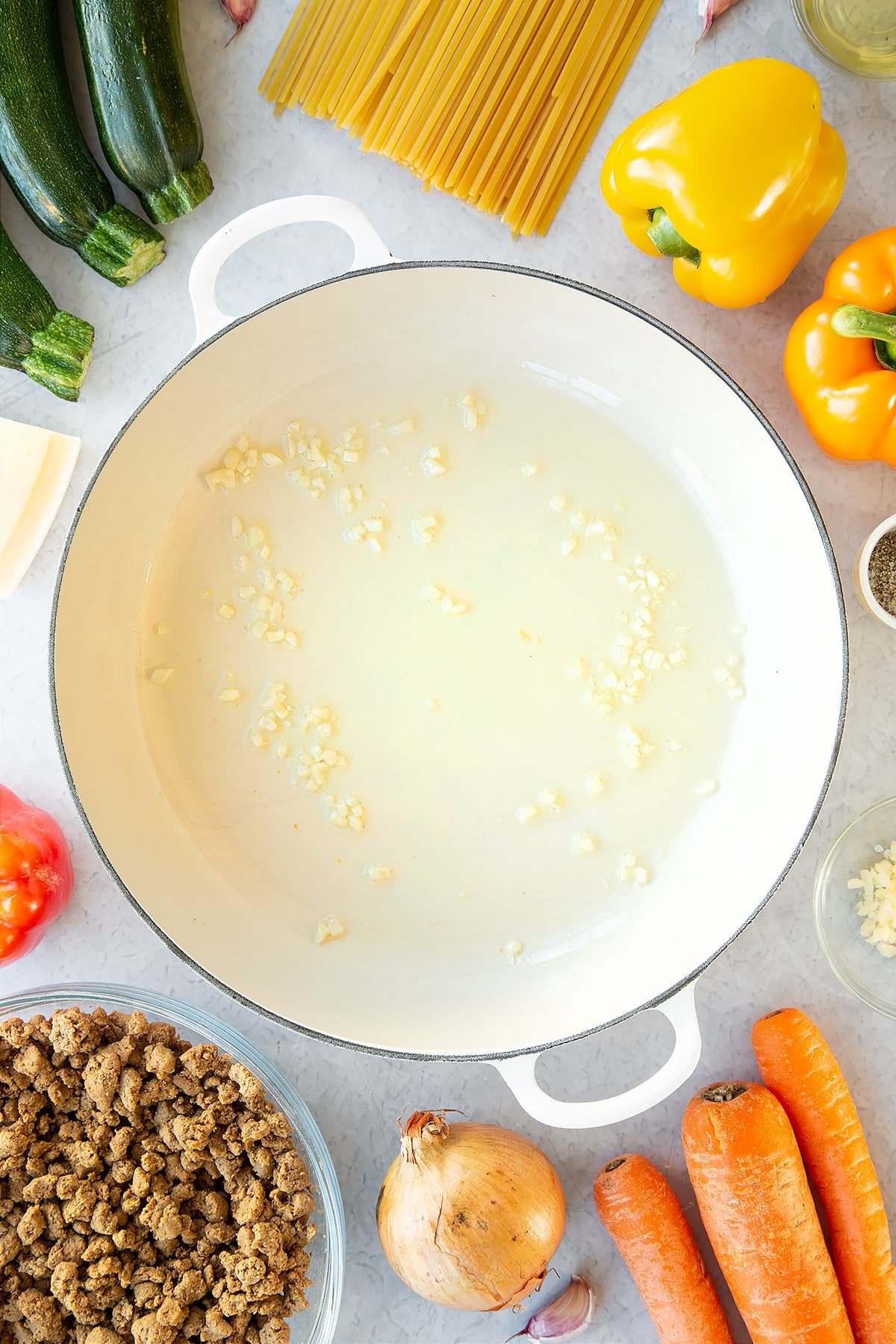 Olive oil and garlic in a large pan. Ingredients to make one pot vegan bolognese surround the pan.