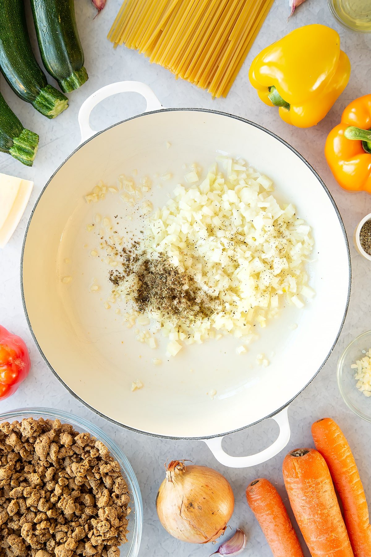 Olive oil, garlic onion and seasoning in a large pan. Ingredients to make one pot vegan bolognese surround the pan.