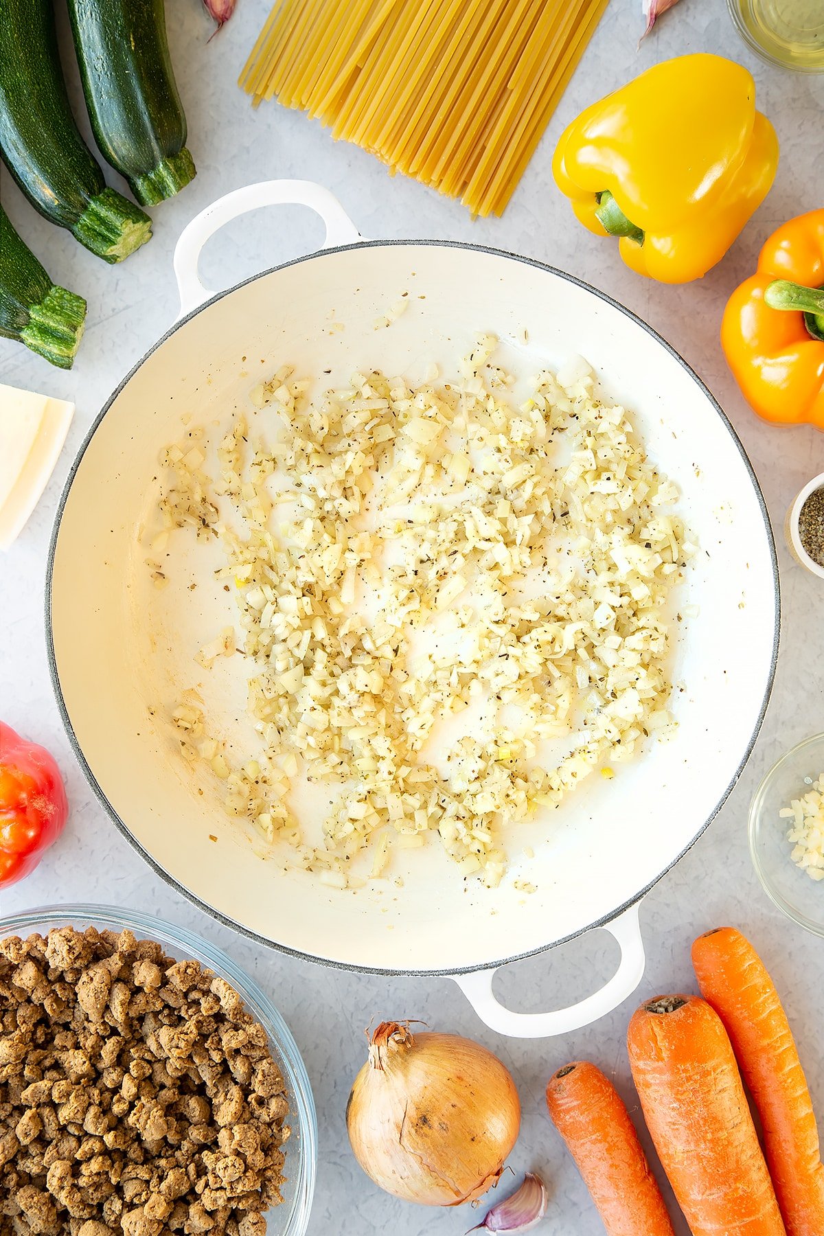 Seasoned garlic and onion sweated in a large pan. Ingredients to make one pot vegan bolognese surround the pan.