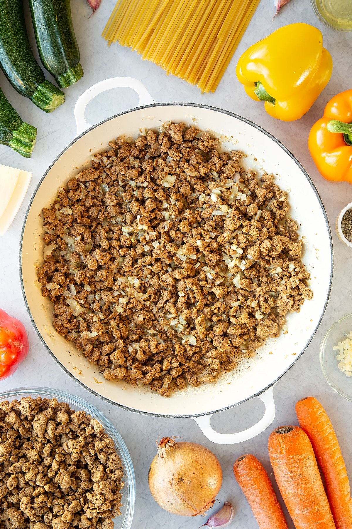 Veggie mince, garlic and onion sweated in a large pan. Ingredients to make one pot vegan bolognese surround the pan.