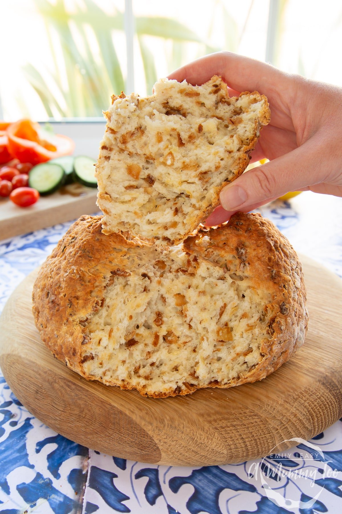 A loaf of onion soda bread on a wooden board. A hand is holding a piece.