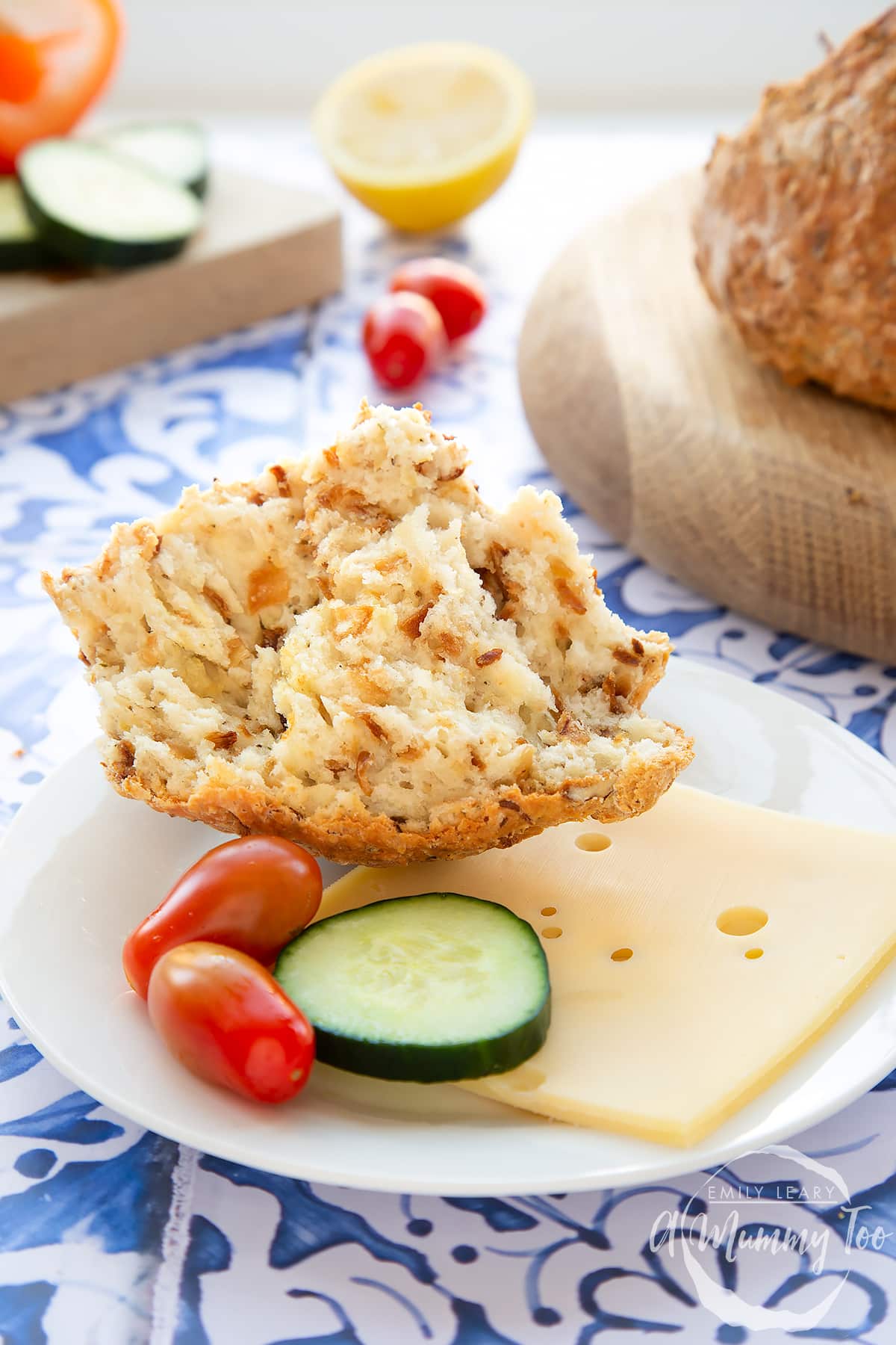 A piece of onion soda bread on a small white plate with sliced cheese, cucumber and cherry tomatoes. 