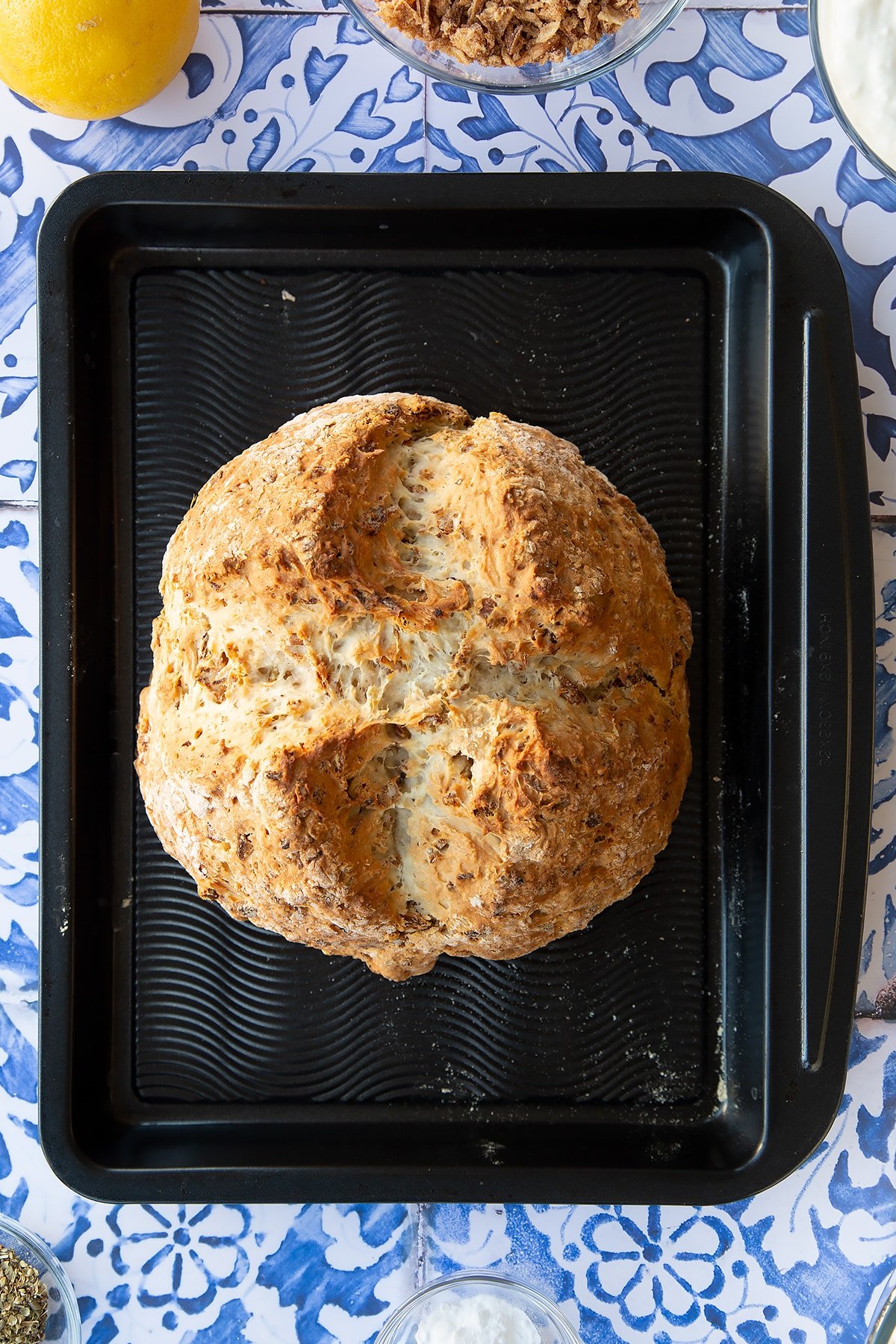 Freshly baked onion soda bread on a baking tray. Ingredients to make onion soda bread surround the tray.