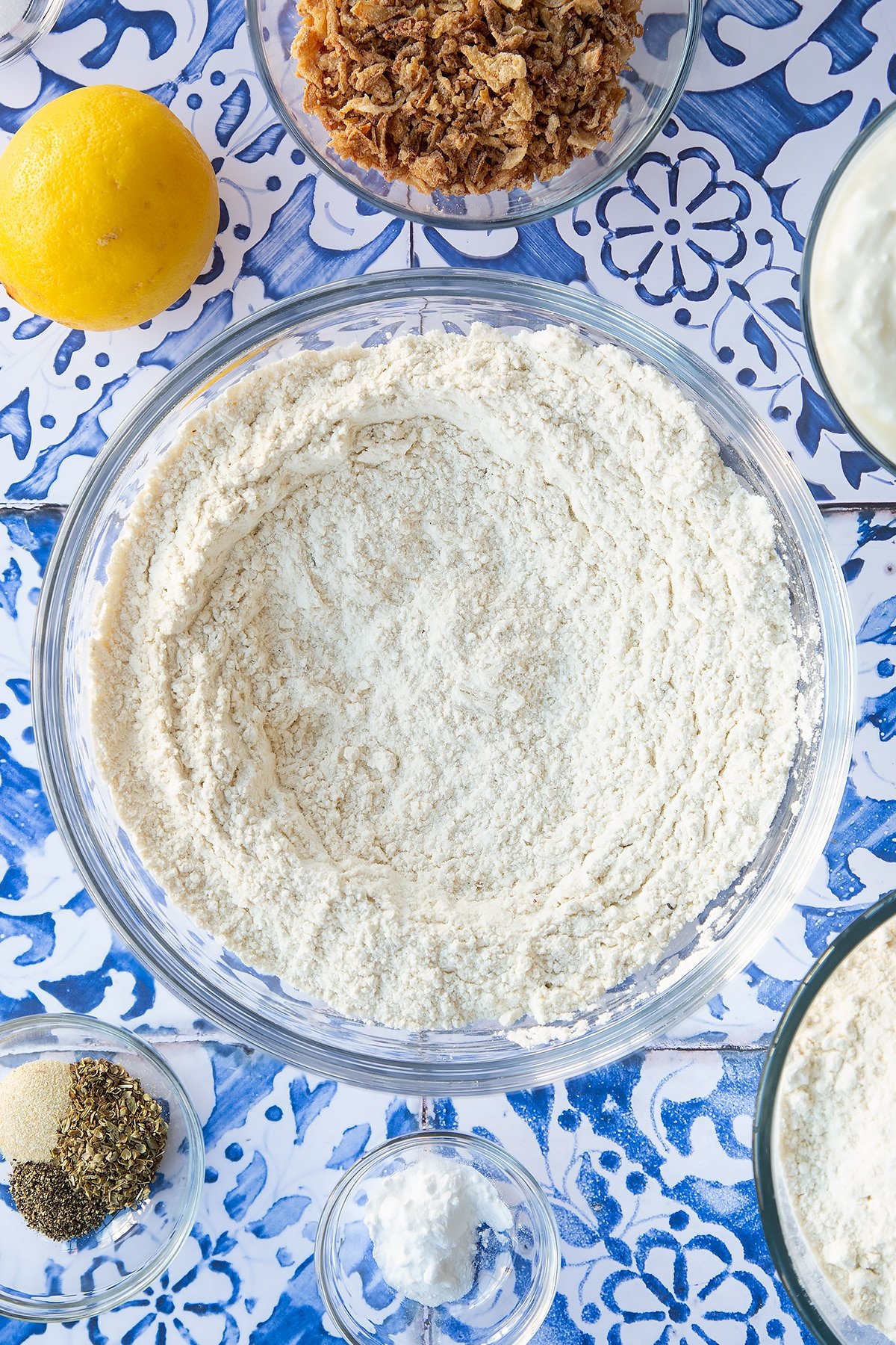 Flour and seasoning stirred together in a mixing bowl. Ingredients to make onion soda bread surround the bowl.