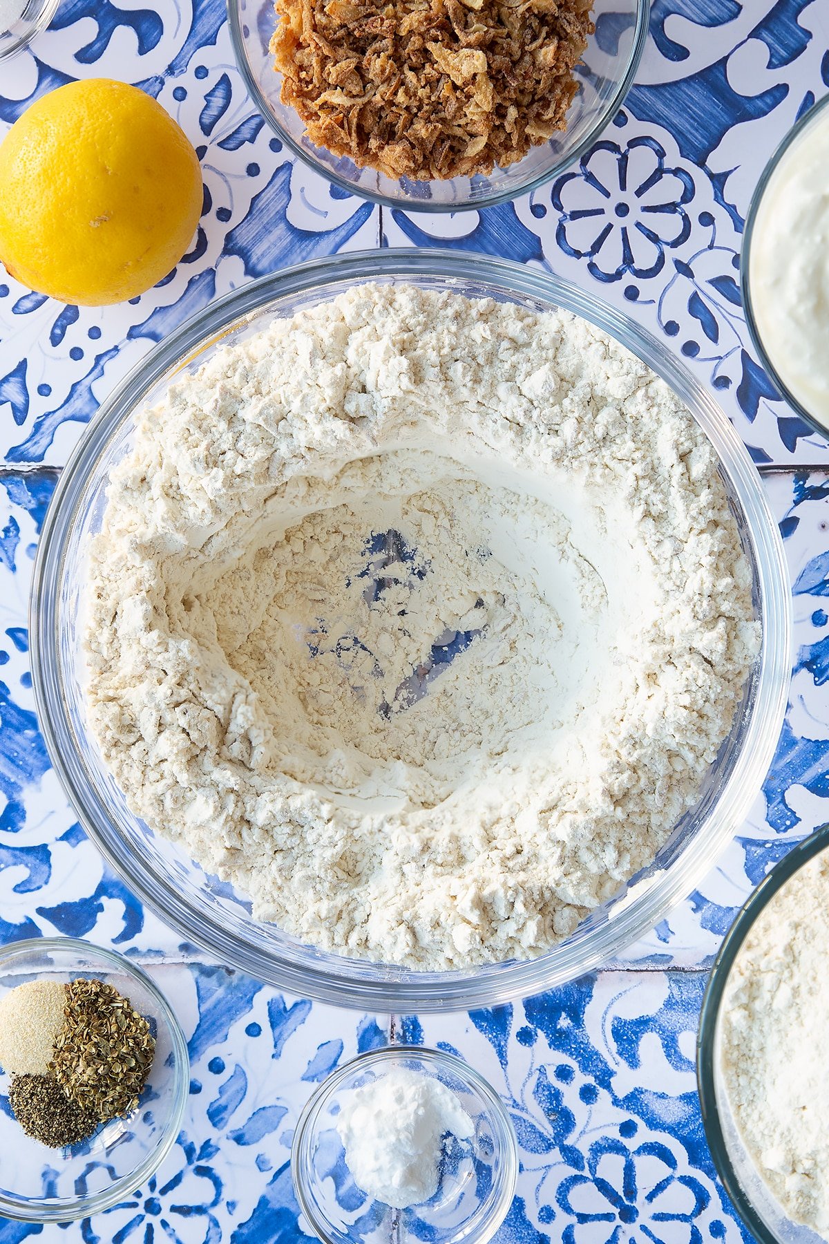 Flour, seasoning and crispy fried onions stirred together in a mixing bowl with a well in teh centre. Ingredients to make onion soda bread surround the bowl.