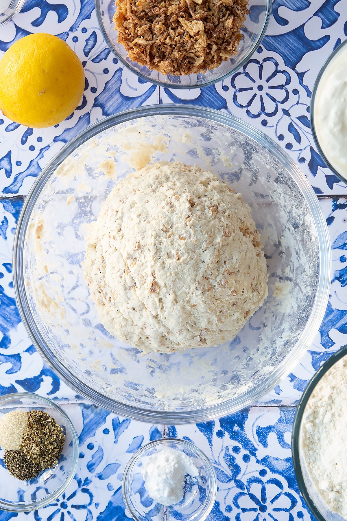 A ball of onion soda bread dough in a mixing bowl. Ingredients to make onion soda bread surround the bowl.