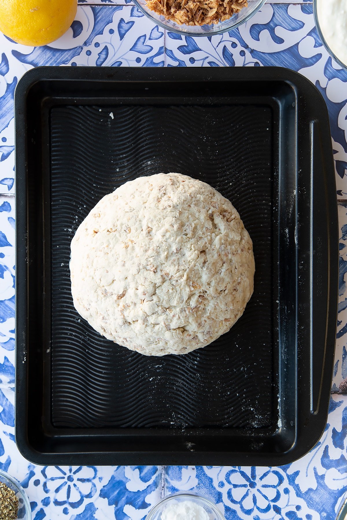 A ball of onion soda bread dough on a baking tray. Ingredients to make onion soda bread surround the tray.