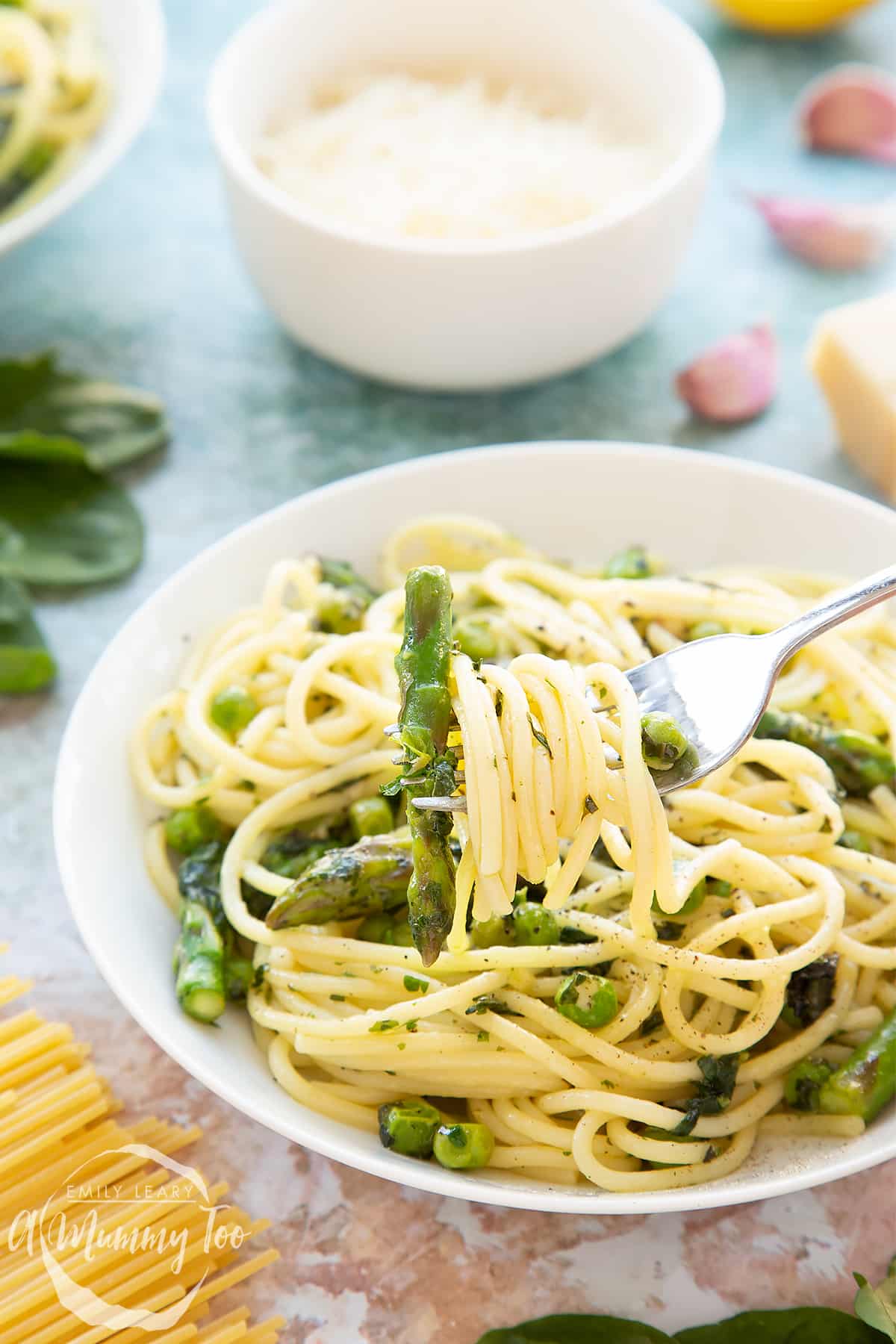 Summer spaghetti with spinach, basil, asparagus and peas, served in a white bowl. A fork wound with spaghetti is in the foreground.