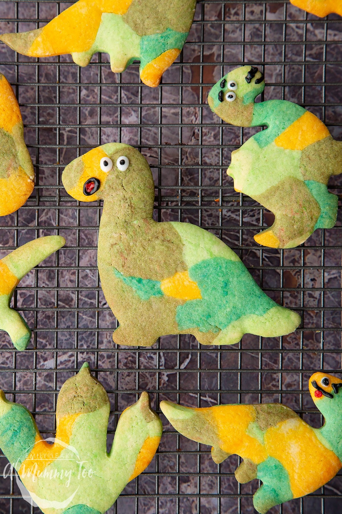 Overhead shot of green dinosaur cookies on a wire rack with the A Mummy Too logo in the corner