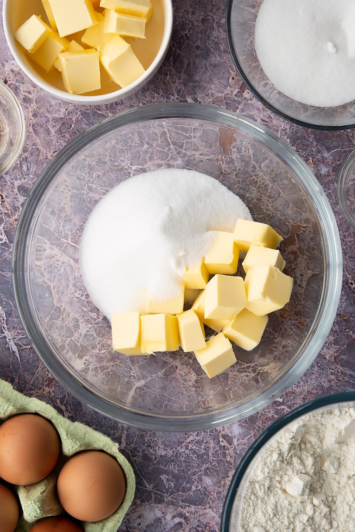 Overhead shot of butter cubes and sugar in a large clear bowl