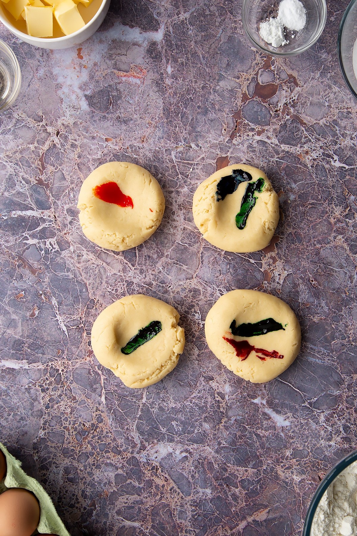 Overhead shot of 4 round pieces of cookie dough with food colouring painted on top