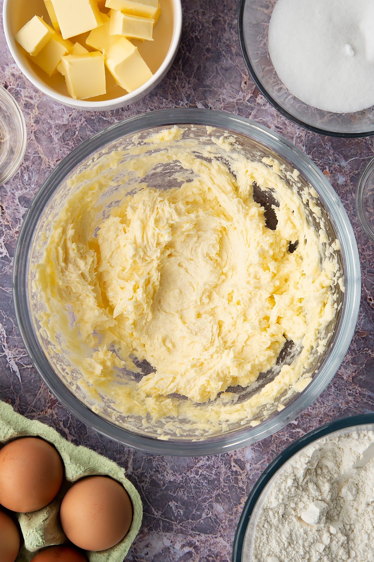 Overhead shot of butter, sugar and egg creamed together in a large clear bowl.