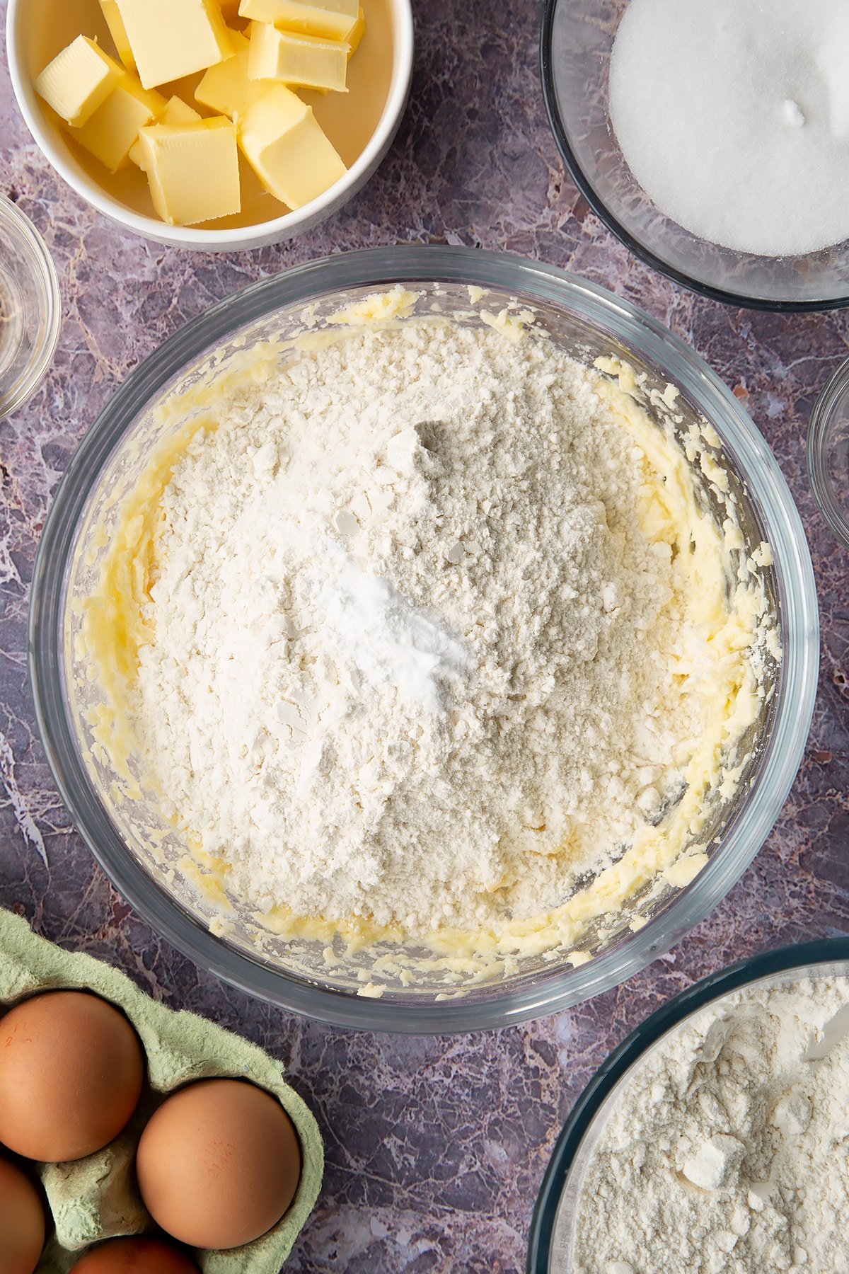 Overhead shot of creamed butter mixture with flour, baking soda and salt in a large clear bowl