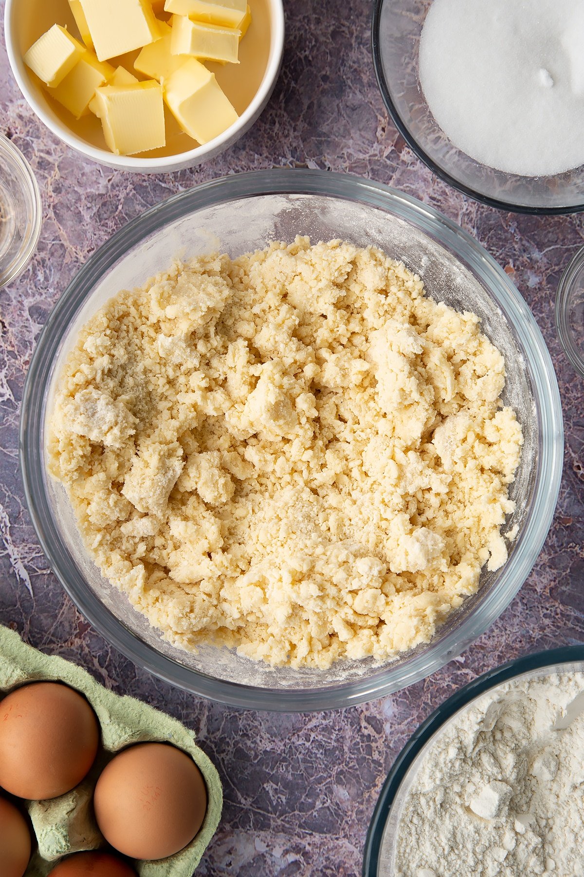 Overhead shot of butter and sugar mixture with flour into crumbs in a large clear bowl