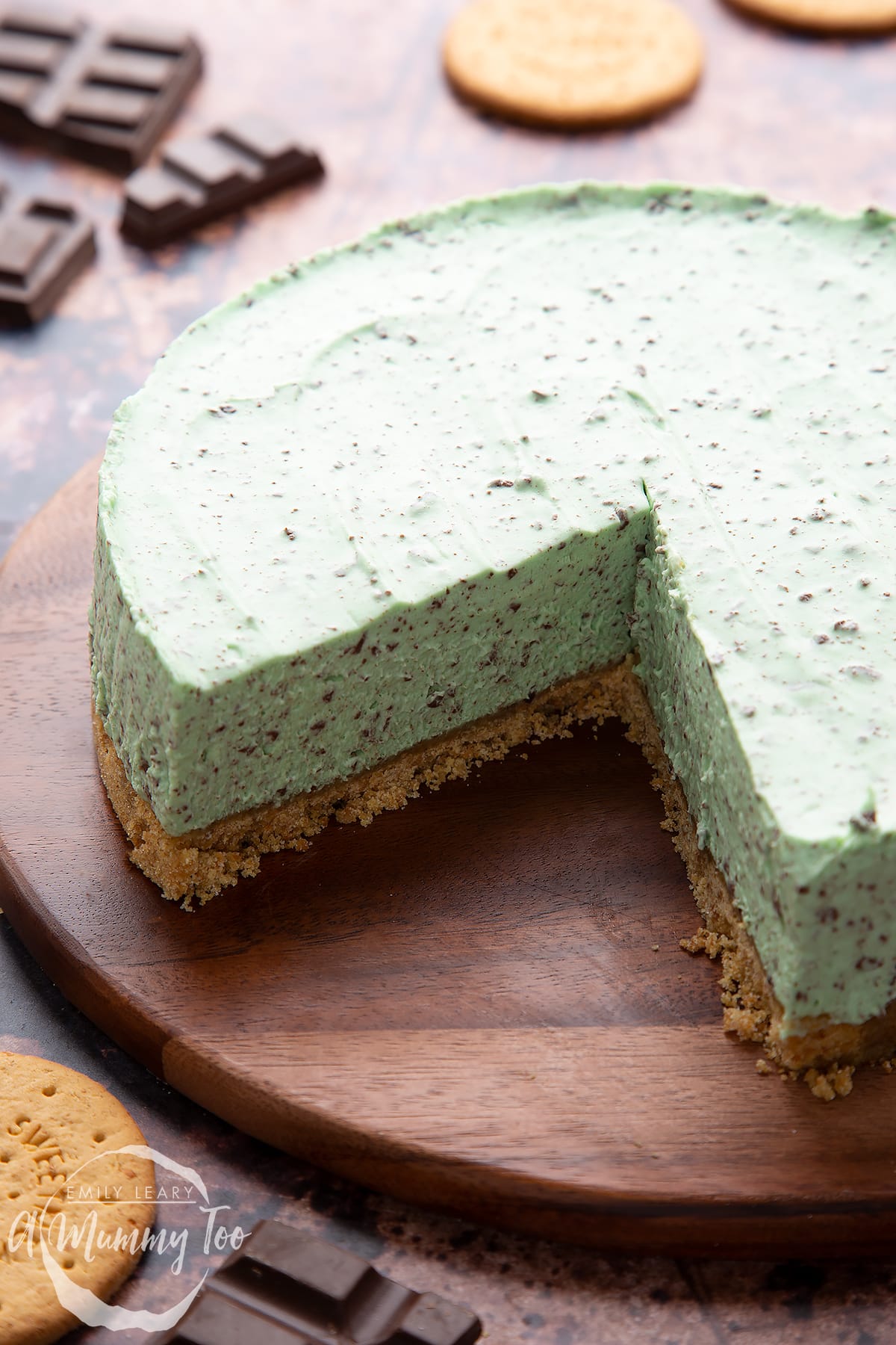 A no bake mint cheesecake with a biscuit base on a wooden board with a large slice removed. 