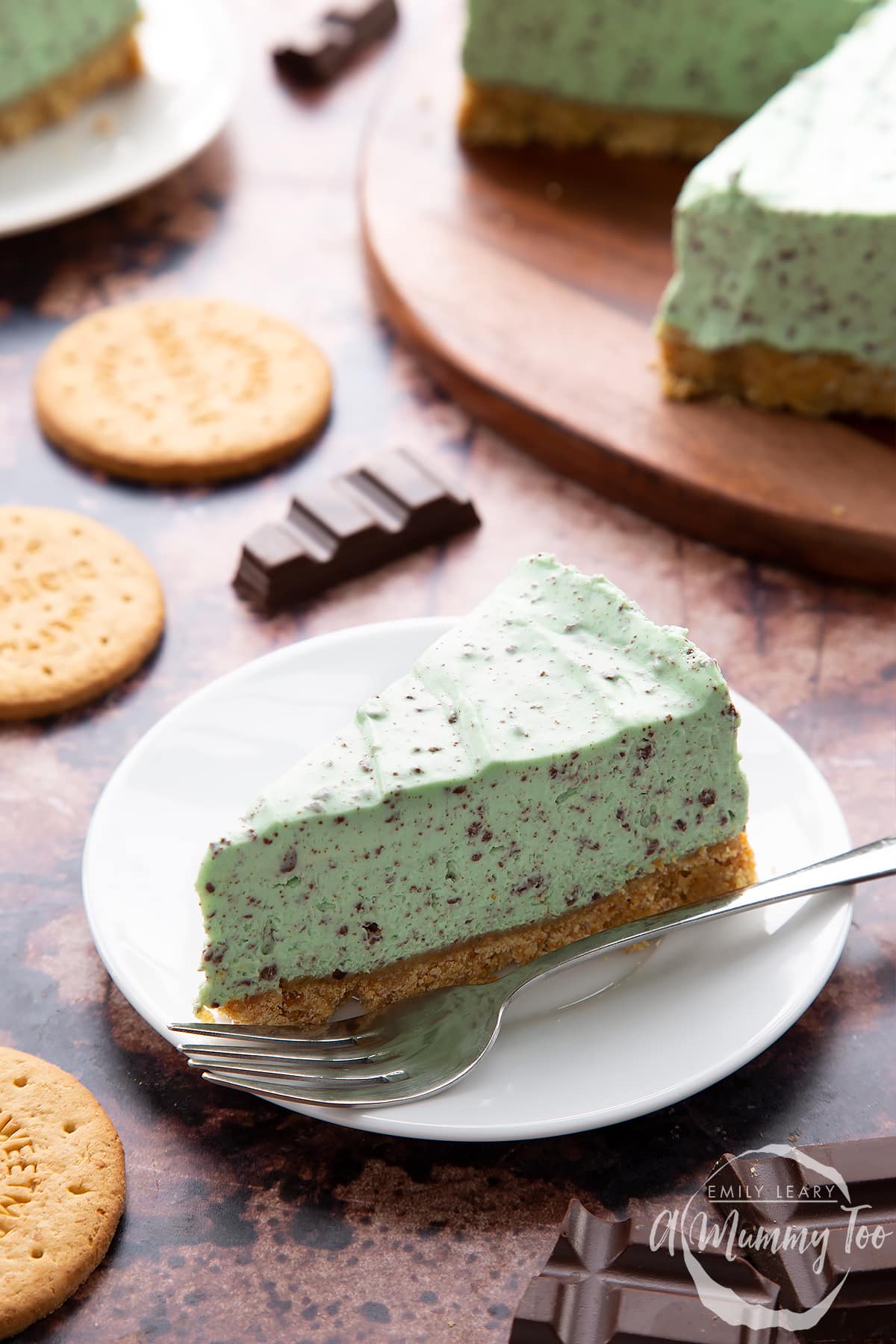A slice of no bake mint cheesecake with a biscuit base on a white plate with a fork.