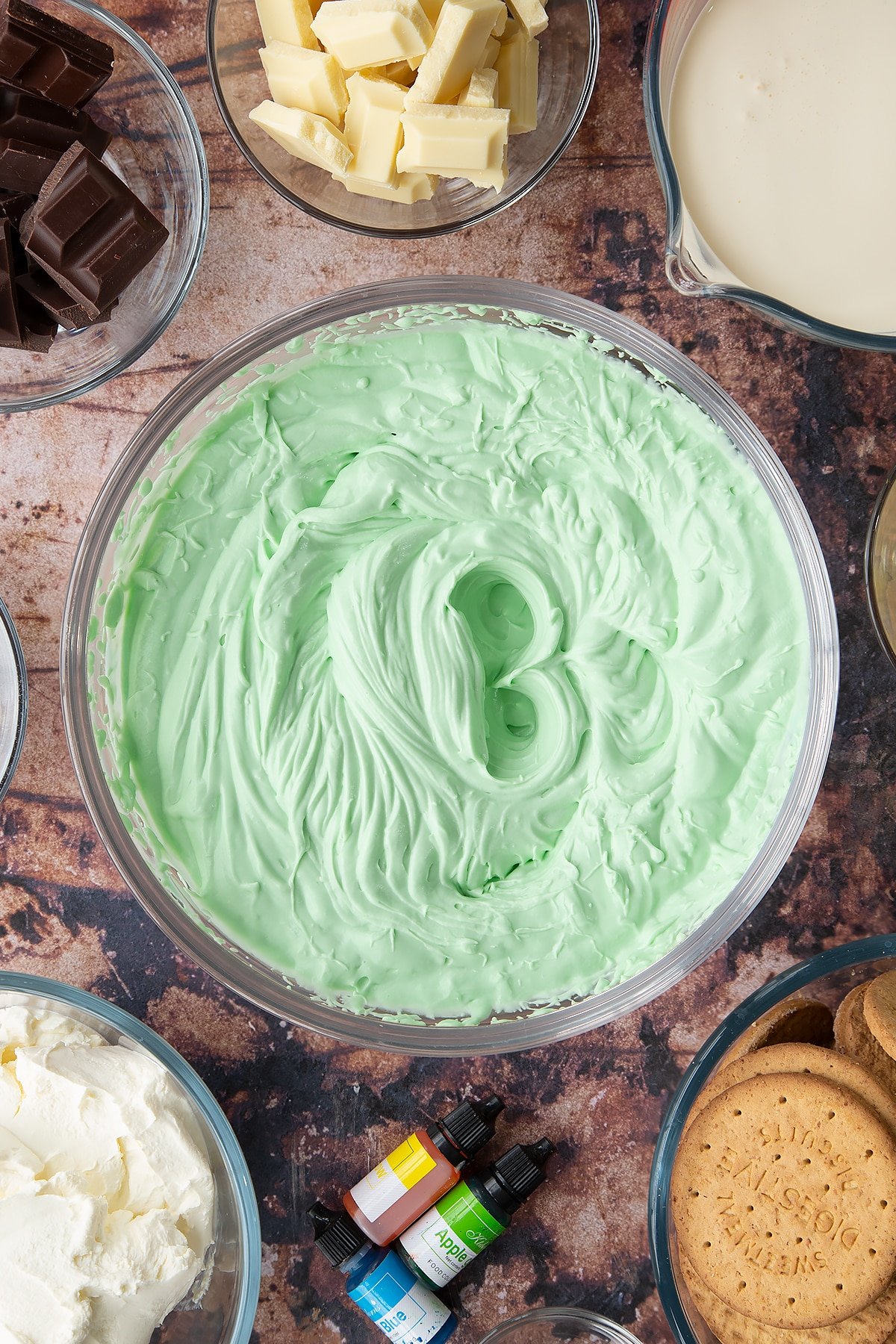 Peppermint green cheesecake filling in a glass bowl. Ingredients to make no bake mint cheesecake surround the bowl.