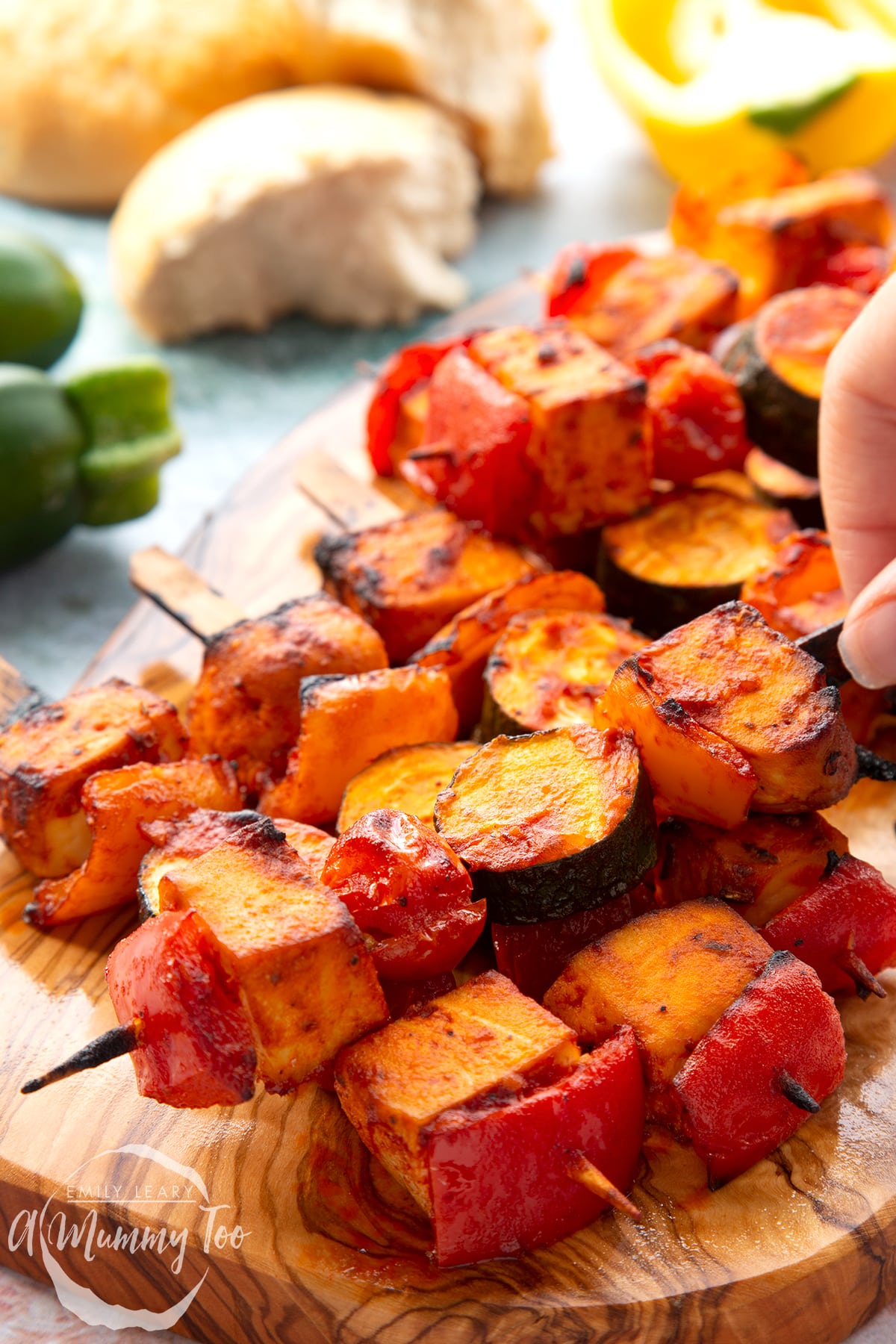 Tofu skewers piled on a wooden board. A hand reaches for one