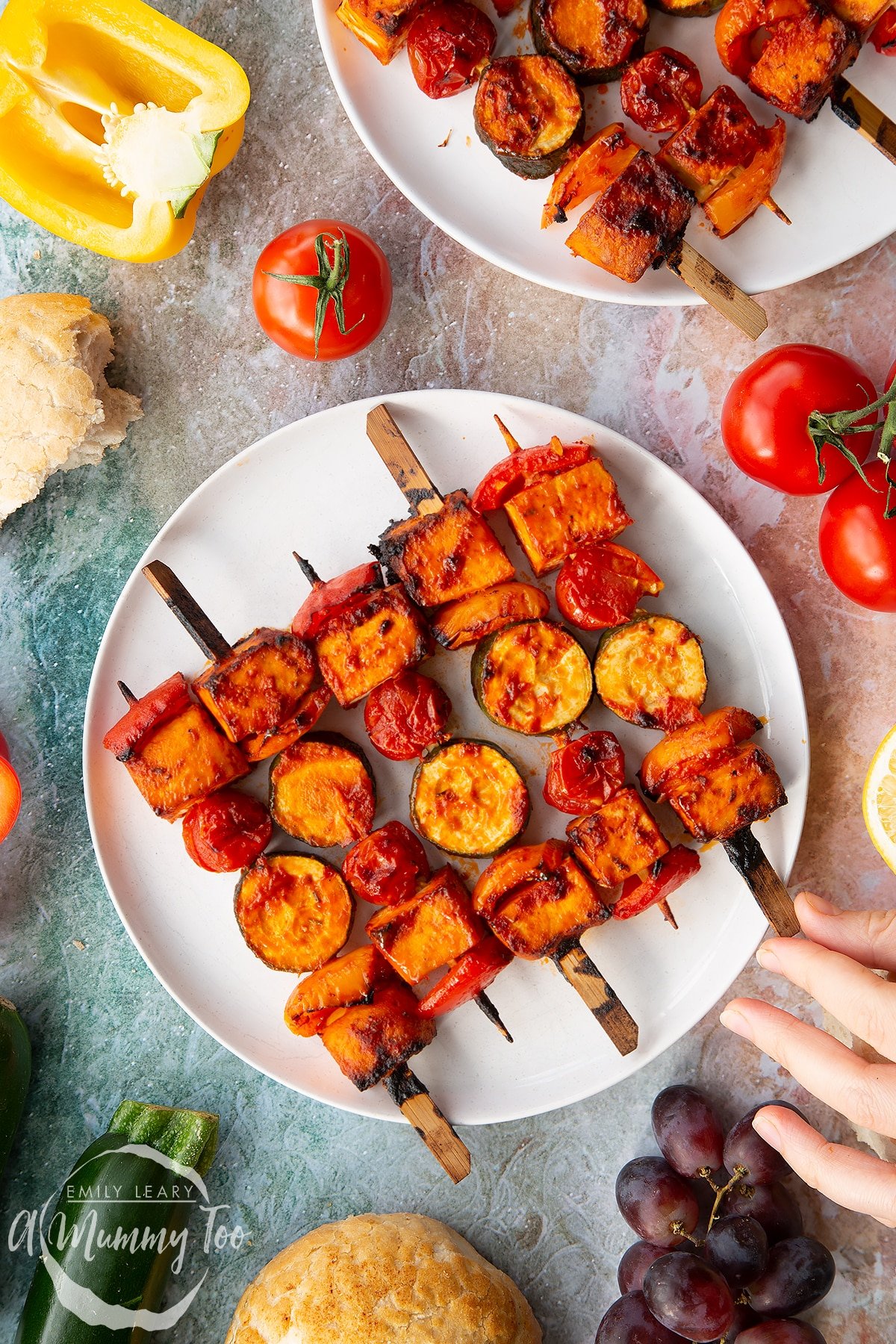 Tofu skewers arranged on a white plate. A hand reaches for one.