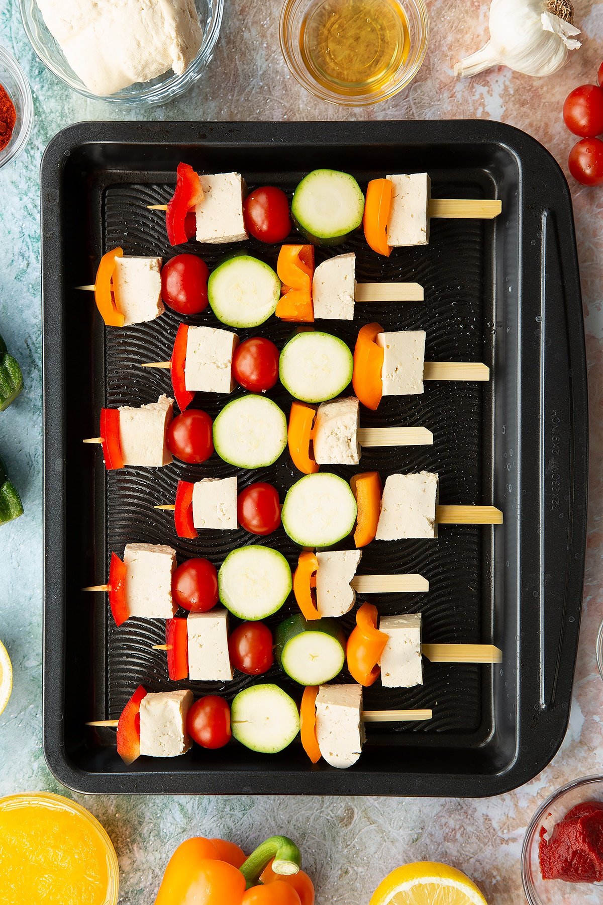 Raw tofu skewers lined up on a baking tray.