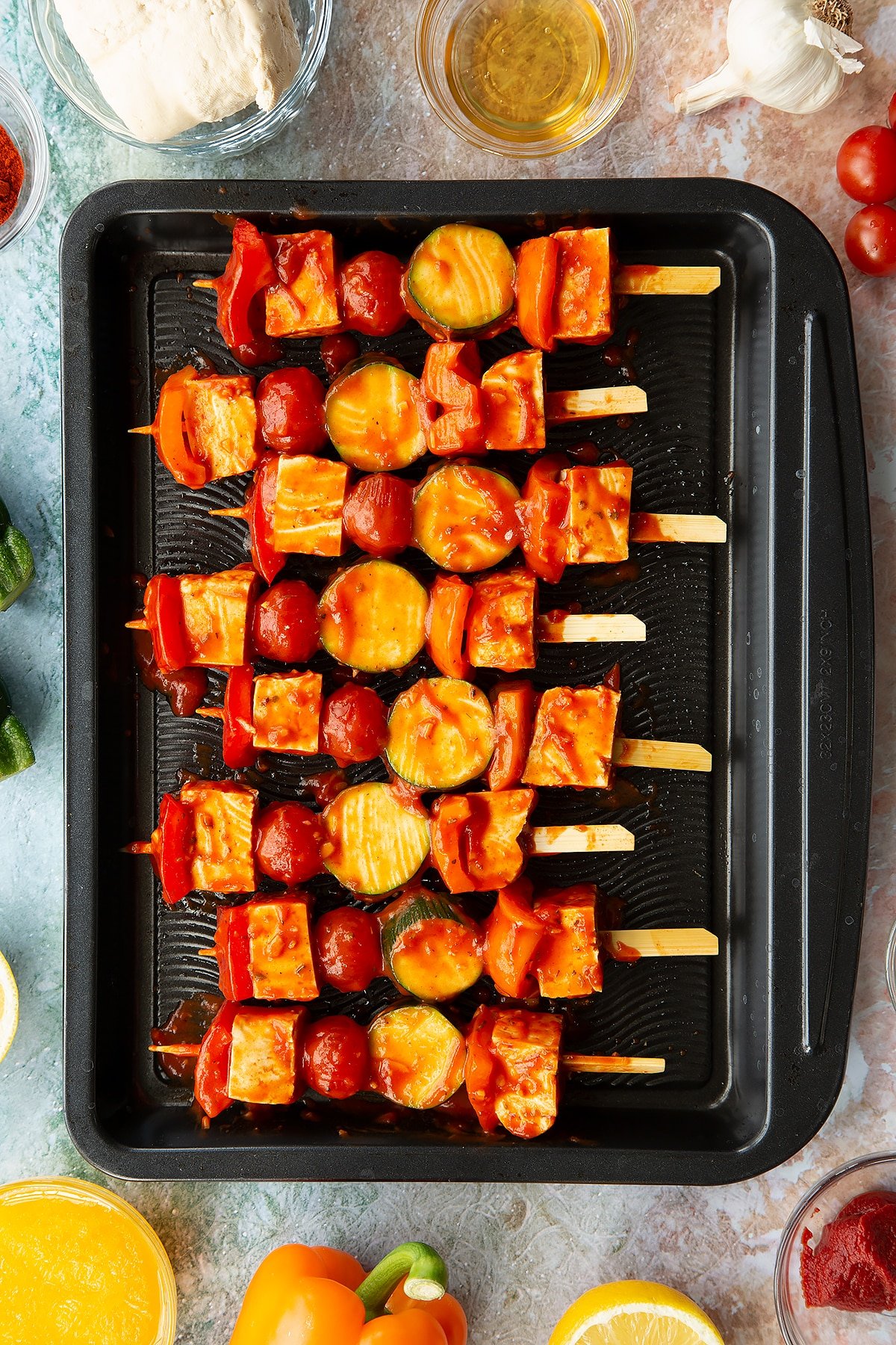 tofu and vegetable kebabs covered in sauce on a metal baking tray.