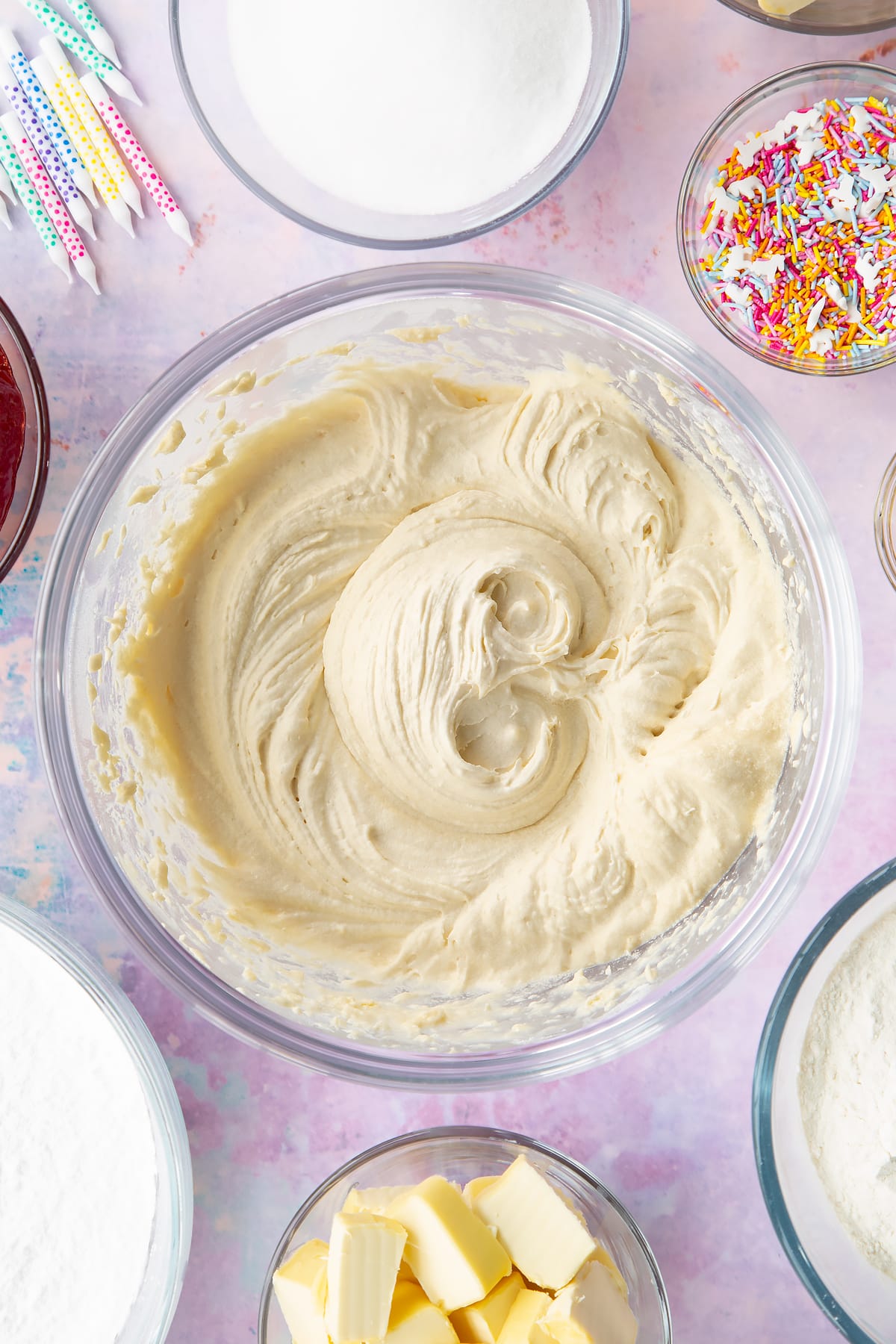 Vegan cake batter in a glass mixing bowl. Ingredients to make vegan birthday cake surround the bowl.