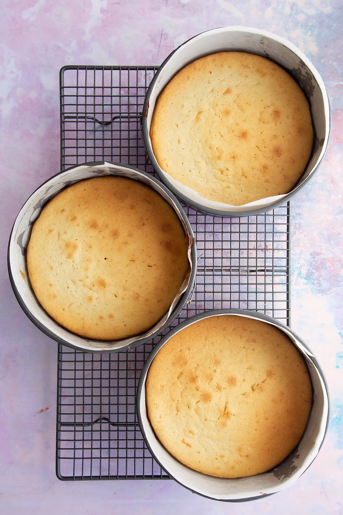 Three vegan cakes in a three lined tins on a wire cooling rack.