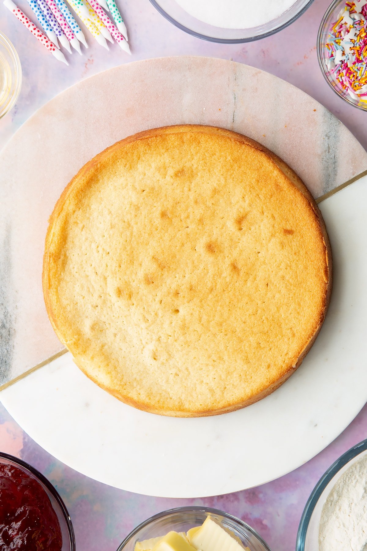 One vegan vanilla sponge on a pink and white round marble board.