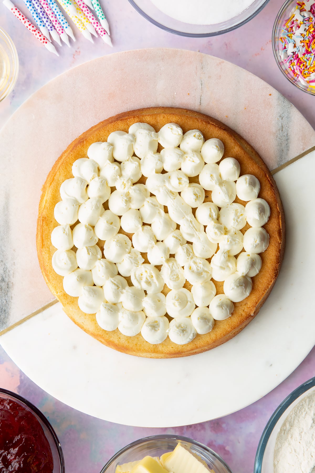 One vegan vanilla sponge with buttercream piped on top on a pink and white round marble board.