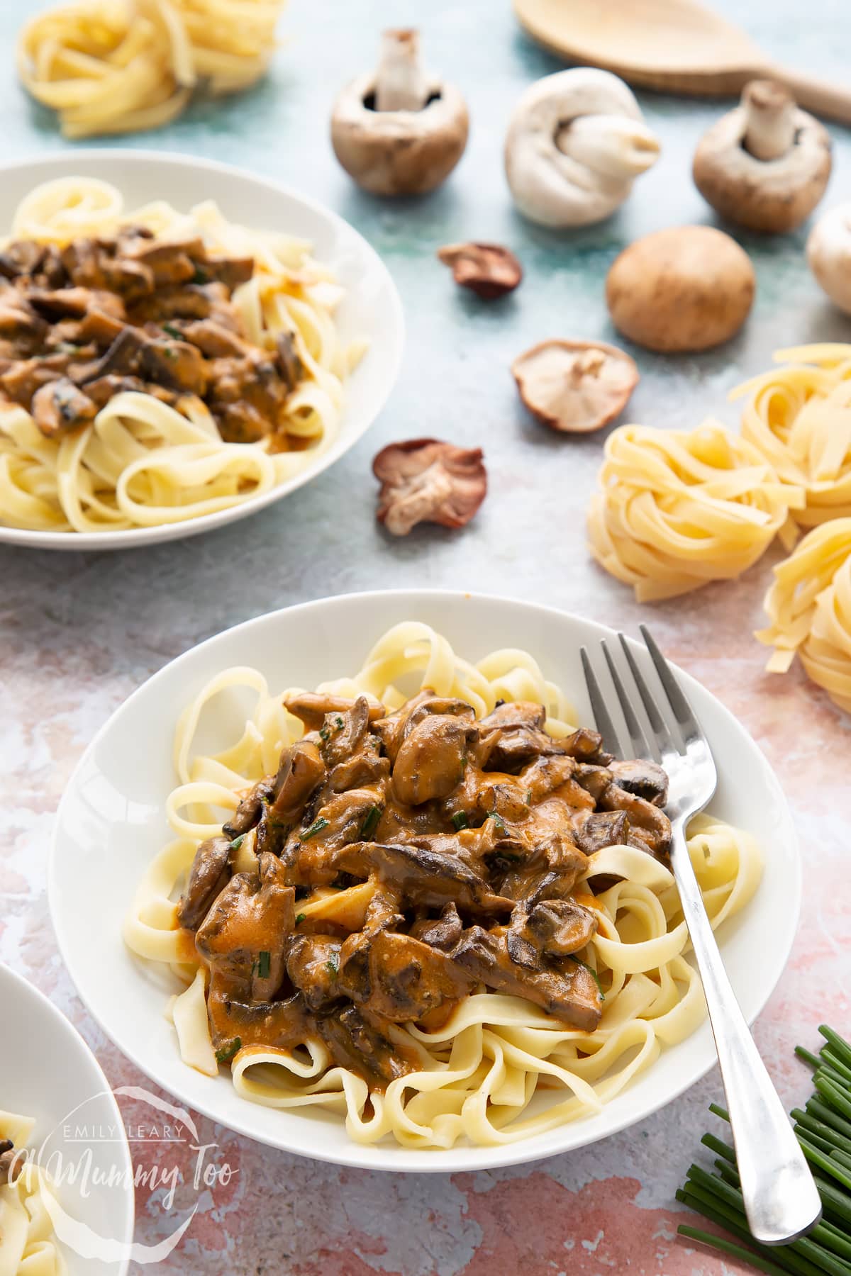 Creamy vegan mushroom stroganoff served in a white bowl with a fork on the side surrounded by ingredients.