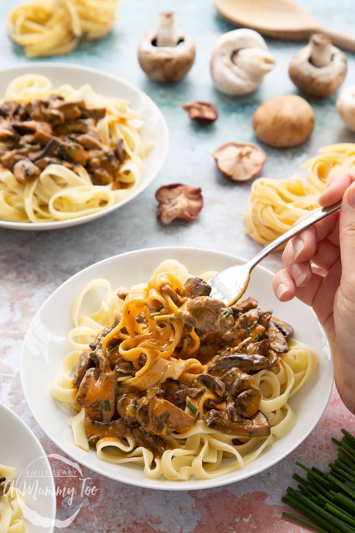 Creamy vegan mushroom stroganoff served in a white bowl with a hand holding a fork pulling up a bite.