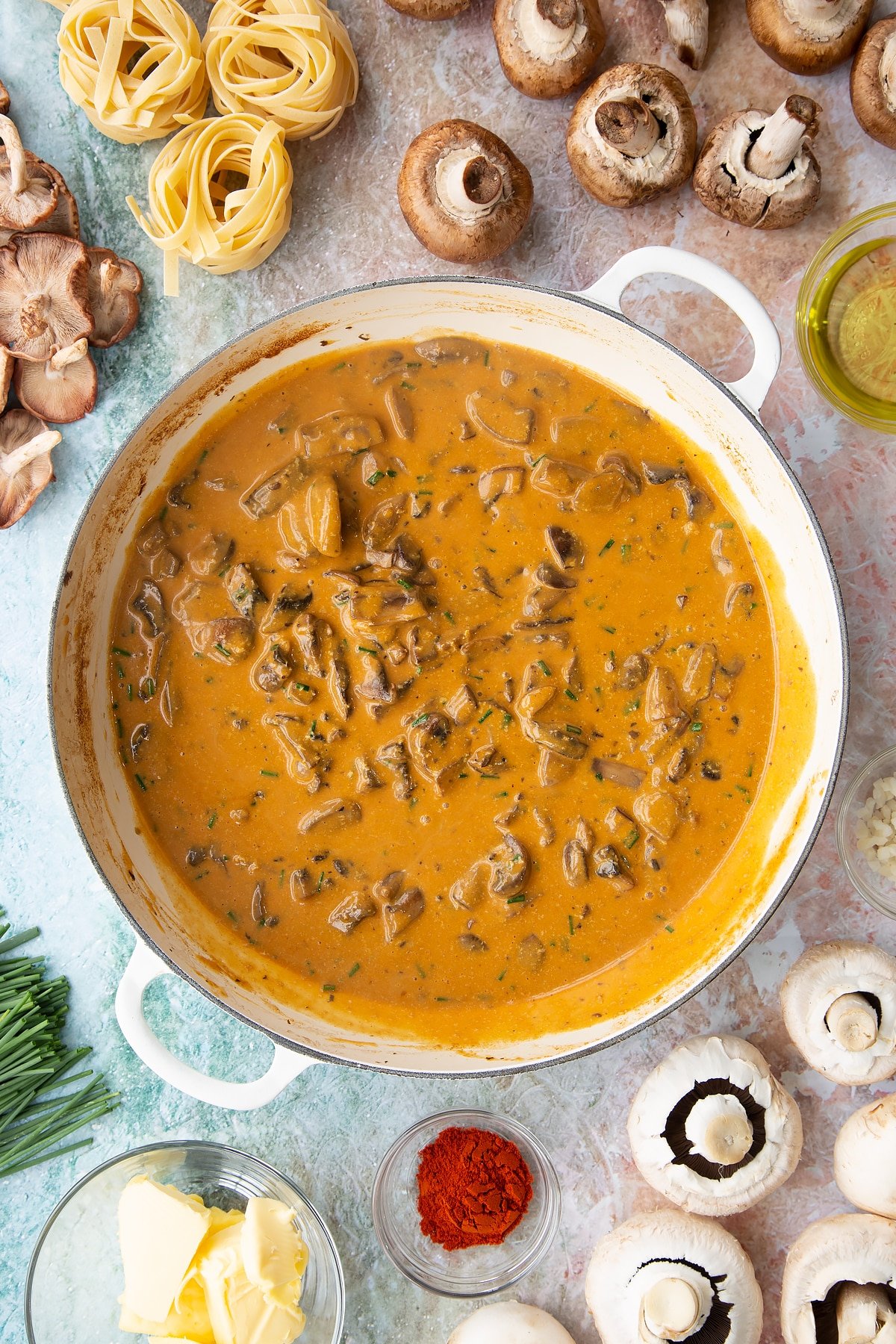 Creamy vegan mushroom stroganoff in a large white pan surrounded by ingredients