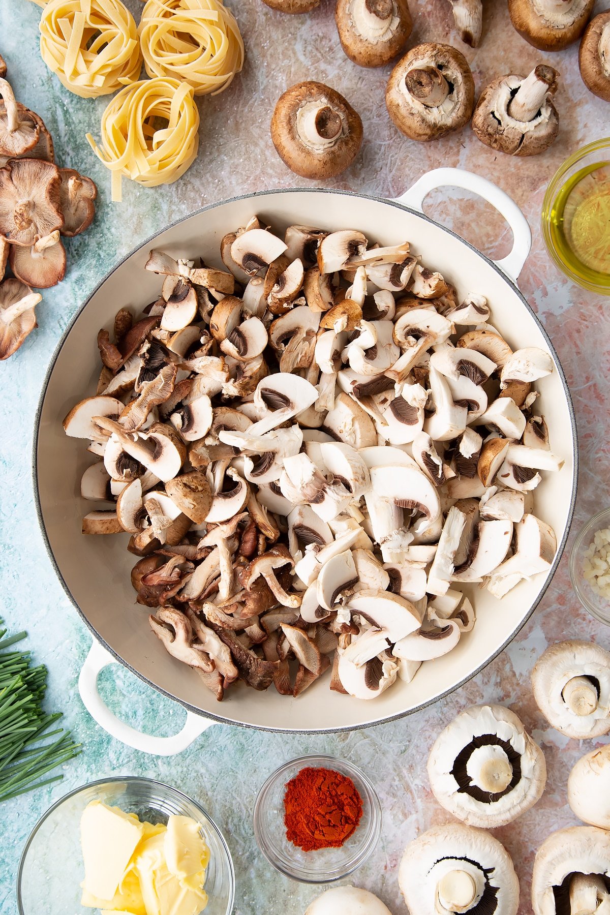 a large white pan with oil in the bottom topped with chopped mushrooms with ingredients surrounding the pan.