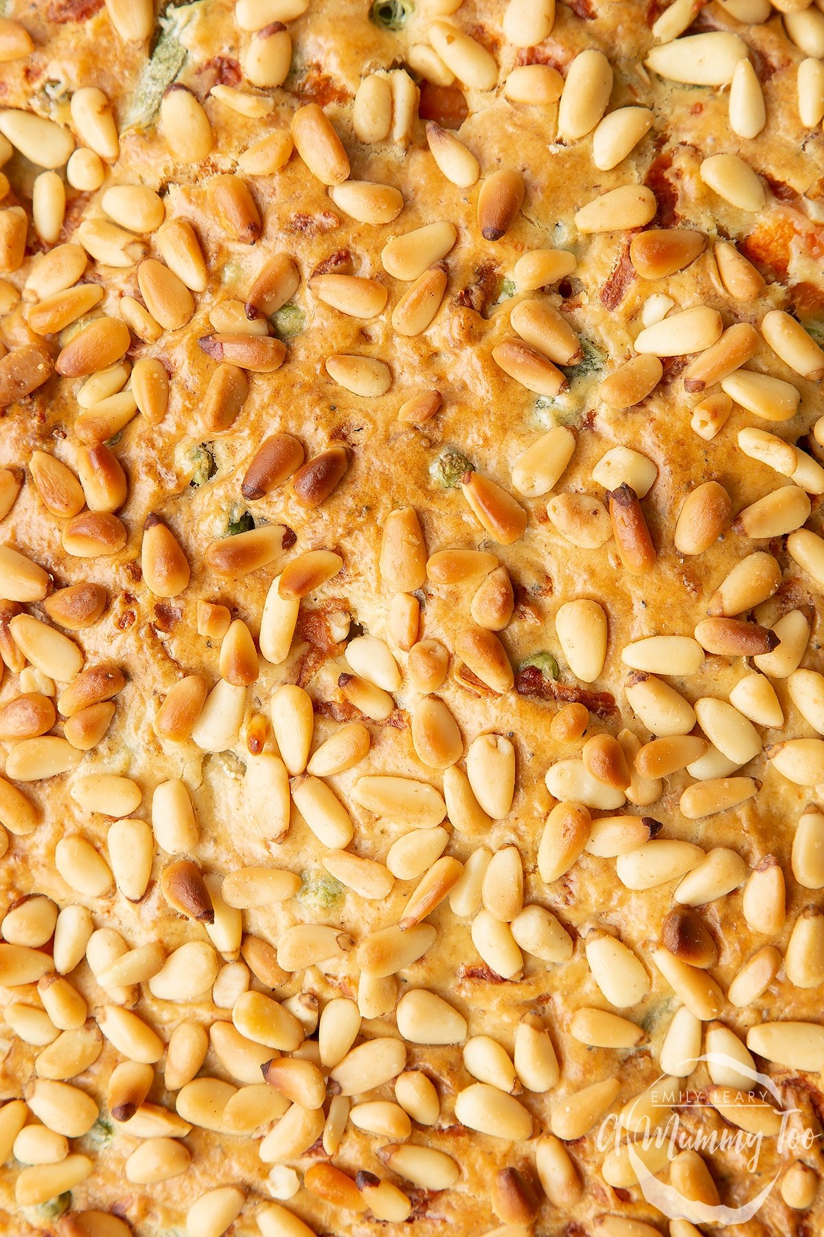 A close up of the top of a vegetable cake topped with pine nuts.