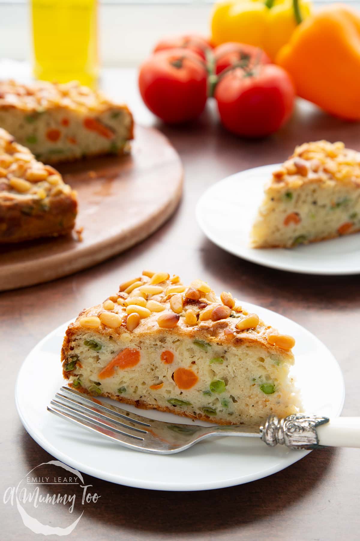 A slice of vegetable cake on a white plate with a fork. There is more cake in the background. 