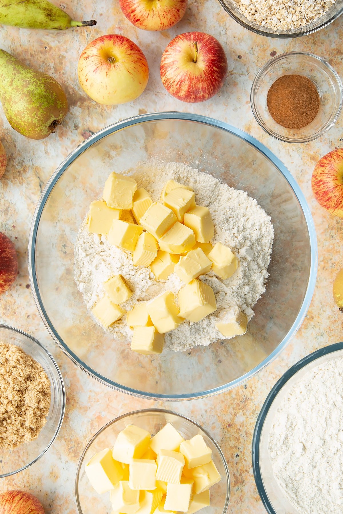 Flour and cold cubed butter in a mixing bowl. Ingredients to make easy apple pear crumble surround the bowl.